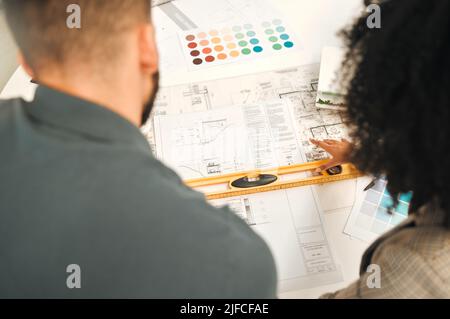 Businesspeople working on a blueprint from above. Two architects working on a building project together. Colleagues using a level during a meeting Stock Photo