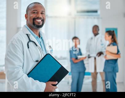 Portrait of a mature african american male doctor holding a folder working at a hospital with colleagues. Expert medical professional smiling ready Stock Photo