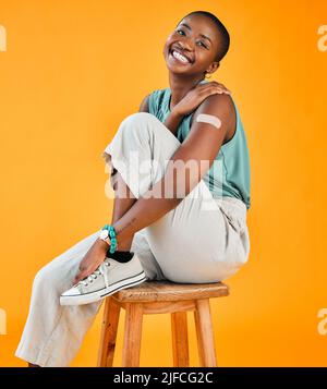 African american covid vaccinated woman showing plaster on arm and smiling. Portrait of black model isolated against yellow studio background with Stock Photo
