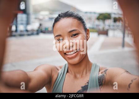 Sporty young mixed race woman with tattoos taking selfies while exercising. Happy young confident female athlete taking a break from her workout or Stock Photo