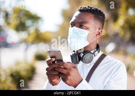 Unrecognizable black man wearing a mask to protect himself from the corona virus pandemic while wearing earphones and texting on a cellphone Stock Photo