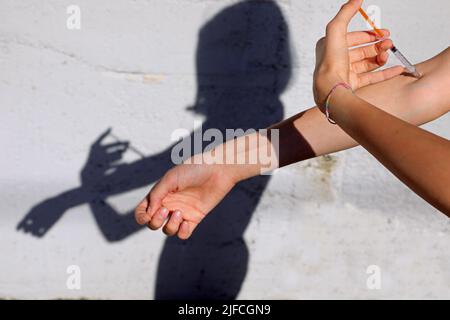 awesome scene of a young drug addict during injection with syringe and shadow on the wall Stock Photo