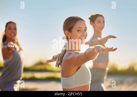 Diverse smiling yoga women in warrior pose during outdoor practice in remote nature. Group of happy active friends bonding and balancing while Stock Photo