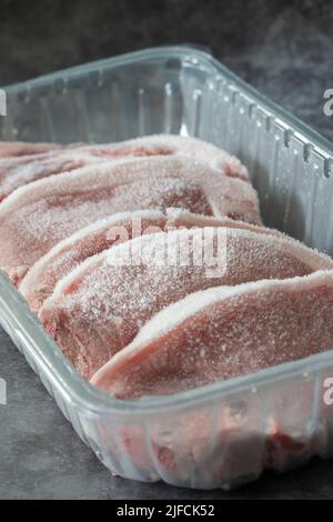 Frozen pork chops in plastic tray packaging thawing.  On a concrete background Stock Photo
