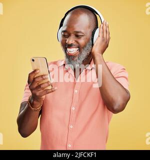 One mature african american man listening to music using wireless headphones while isolated against a yellow background. Happy man with a grey beard Stock Photo
