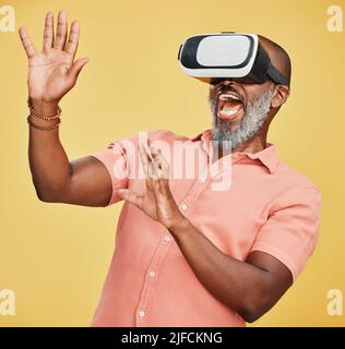 One mature african american man using a virtual reality headset while standing in studio isolated against a yellow background. Handsome man with a Stock Photo
