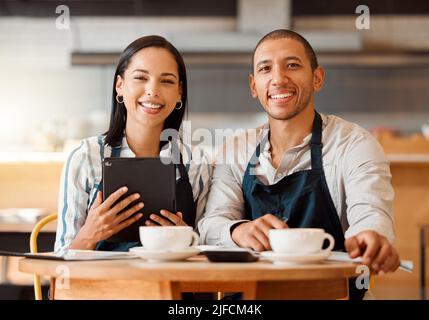 Two restaurant workers planning on a digital tablet in a small business. Young mixed race colleagues having coffee while reviewing plans in a cafe Stock Photo