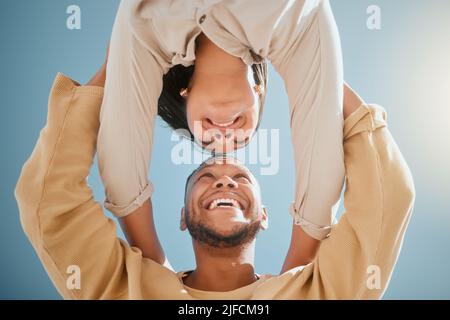 Happy young mixed race couple facing each other while standing with their hands on each others shoulders and smiling against a blue sky, from below Stock Photo