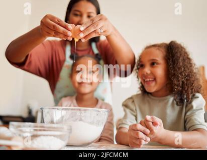 Females only, happy mixed race family of three cooking in a messy kitchen together. Loving black single parent bonding with her daughters while Stock Photo