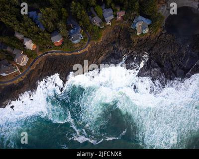 Shooting from a drone. A small green city on a hilly green ocean shore. Beautiful seascape. The waves of the raging ocean crash against the shore. Eco Stock Photo