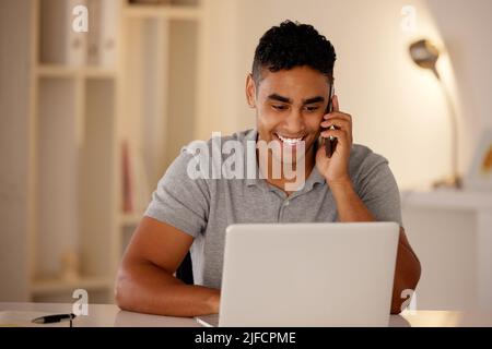Man working remotely using a laptop and talking on a cellphone. Businessman working from home. Happy male doing freelance work while on a call Stock Photo