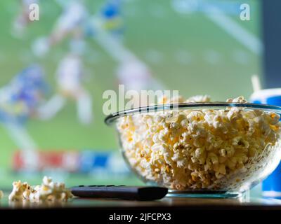 A sports program on the TV screen, a large bowl of popcorn and a TV remote control. Close-up. Rest in front of TV sports fan, fast food. Advertising, Stock Photo