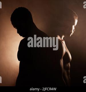 Two handsome, muscular young african american men in studio against a dark background. Macho male athletes looking thoughtful isolated on black Stock Photo
