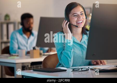 One happy young caucasian call centre telemarketing agent talking on a headset while working on a computer in an office. Confident and friendly Stock Photo
