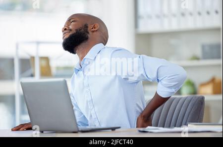 Unhappy african american businessman suffering from bad back pain in an office at work alone. One tired male business professional touching his sore Stock Photo