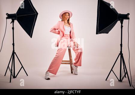 Portrait of a young mixed race female posing in trendy fashionable clothing while chilling on a chair in a studio shoot. Hispanic woman showing the Stock Photo