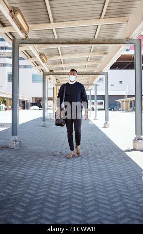 Black businessman travelling alone.A african american businessman walking around town with his luggage while wearing mask to protect himself from the Stock Photo