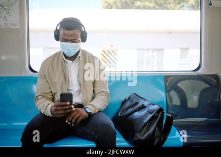 Black businessman travelling alone. A young african american businessman using a cellphone and listening to music on his wireless headphone while Stock Photo