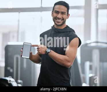 Portrait of smiling asian trainer alone in gym showing cellphone screen. Coach standing, promoting discount and deal for workout in health club. Young Stock Photo