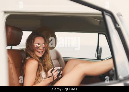 Places to go, memories to make. Shot of a young woman using a camera on a road trip in her van. Stock Photo