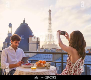 A view worth waking up to. Shot of a young couple having breakfast on the balcony of an apartment overlooking The Eiffel Tower in Paris, France. Stock Photo