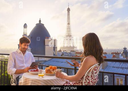 Nothing says honeymoon like a trip to Paris. Shot of a young couple having breakfast on the balcony of an apartment overlooking The Eiffel Tower in Stock Photo