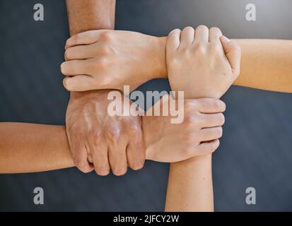 Closeup of diverse group of people from above holding each others wrists in a circle to express unity, support and solidarity. Connected hands of Stock Photo