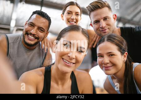 Portrait of a diverse group of happy sporty people taking selfies while exercising together in a gym. Cheerful motivated athletes excited and ready Stock Photo