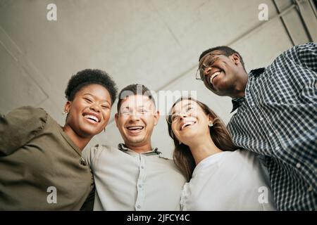 Team of happy united young business people hugging each other. Diverse mixed race group of men and women standing in row in their office, huddling and Stock Photo