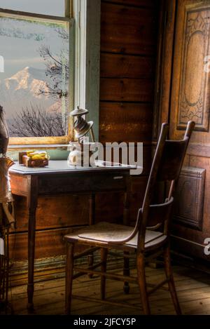 What was it like in 1890 when soft sunlight warmed these wood paneled walls, a work table, and chair next to window in Garnet Ghost Town, Montana? Stock Photo