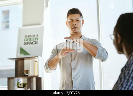 Young mixed race businessman talking and doing a presentation in a meeting at work. Hispanic male boss planning with colleagues during a workshop Stock Photo