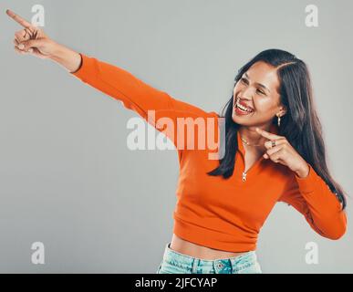 Smiling mixed race woman isolated on grey studio background with copyspace and pointing. Beautiful happy young hispanic standing alone and feeling Stock Photo