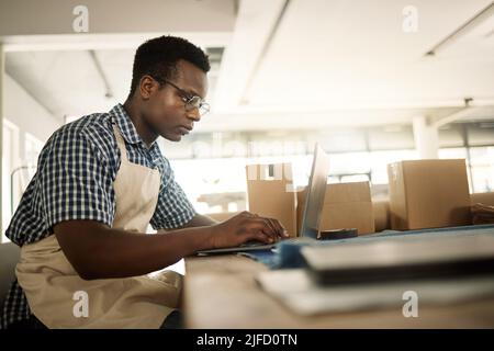 Focused businessman typing an email. Young fashion designer working on his laptop. Creative entrepreneur working in his design workshop. African Stock Photo