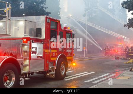 Seattle - June 30, 2022; Seattle fire department fighting an active fire in a smokey scene using ladder trucks and hoses with water streams Stock Photo