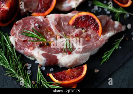 Raw pork steaks with rosemary and orange marinated on a stone board. Cooking meat steaks. Stock Photo