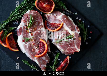 Raw pork steaks with rosemary and orange marinated on a stone board. Cooking meat steaks. Stock Photo