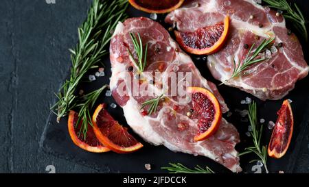 Raw pork steaks with rosemary and orange marinated on a stone board. Cooking meat steaks. Stock Photo