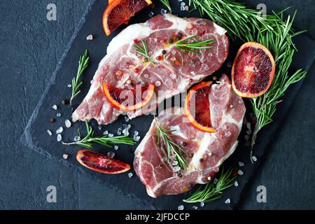 Raw pork steaks with rosemary and orange marinated on a stone board. Cooking meat steaks. Stock Photo