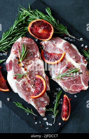 Raw pork steaks with rosemary and orange marinated on a stone board. Cooking meat steaks. Stock Photo