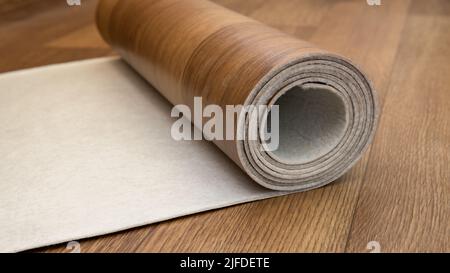 An expanded roll of brown linoleum. Close-up side view. Linoleum with wood structure lies on the floor. Home interior. Construction work at home. Stock Photo