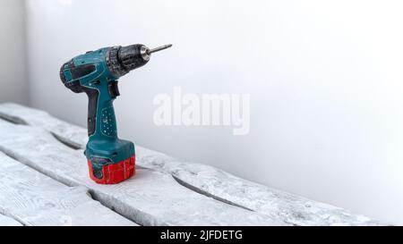 An electric screwdriver stands on a white wooden stand from boards near a white wall. Construction work at home. DIY repair Stock Photo