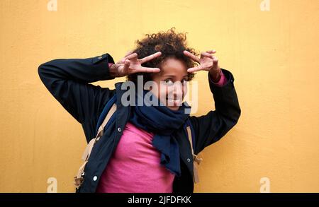 A beautiful curly-haired African-American female showing peace on an orange background Stock Photo