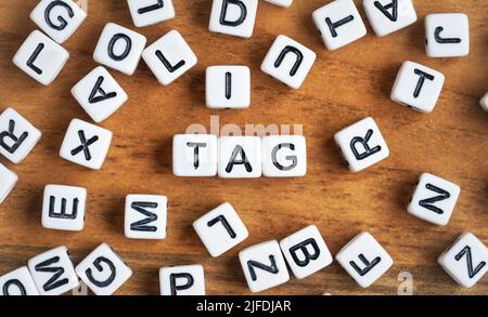 Small white and black bead cubes on wooden board, letters in middle spell TAG Stock Photo