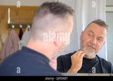 Man checking out his neatly trimmed beard in the mirror running his fingers over the hair in an over the shoulder view Stock Photo