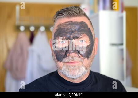 Senior bearded man using a cosmetic face mask in a close up headshot for a skin care concept Stock Photo