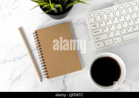 Office desk with brown notepad, cup of coffee, pencil and computer keyboard on top of marble desk Stock Photo