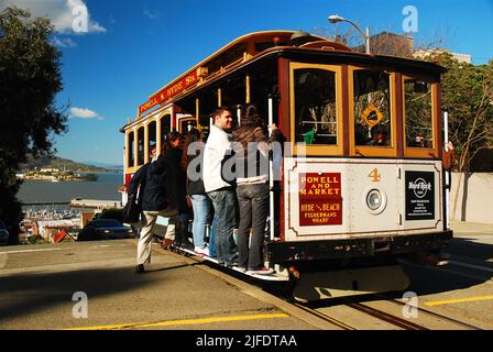 A San Francisco cable car crests the top of Russian Hill stopping to allow passengers on and off on Hyde Street with Alcatraz Island in the background Stock Photo
