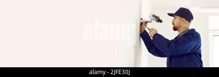 Portrait of busy technician at work. Young man installing or repairing security camera, surveillance system in modern office or apartment. Stock Photo