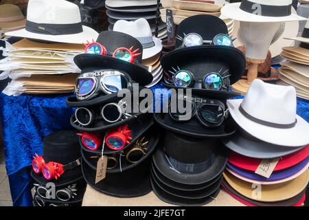 Display of hats for sale on a market stall during Winchester Hat Fair event, including black steampunk hats with goggles or glasses, England, UK Stock Photo