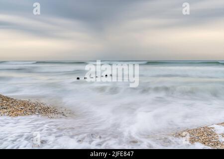 Milky, pastel shade seas, swirling around the beach and old groin at Medmerry near Selsey in West Sussex Stock Photo